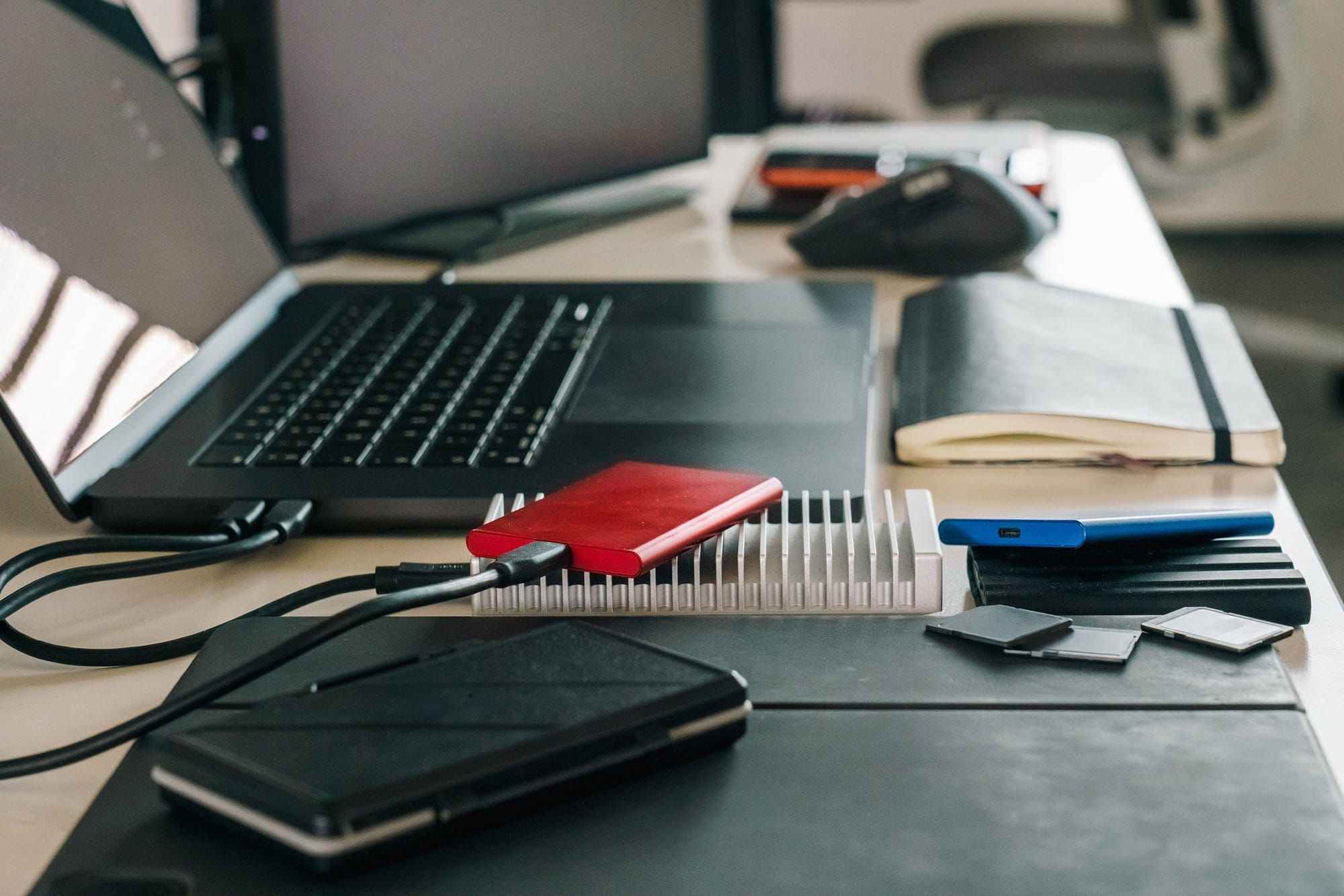 Portátil con varios discos externos conectados, un SSD azul y tarjetas de memoria sobre una mesa de trabajo