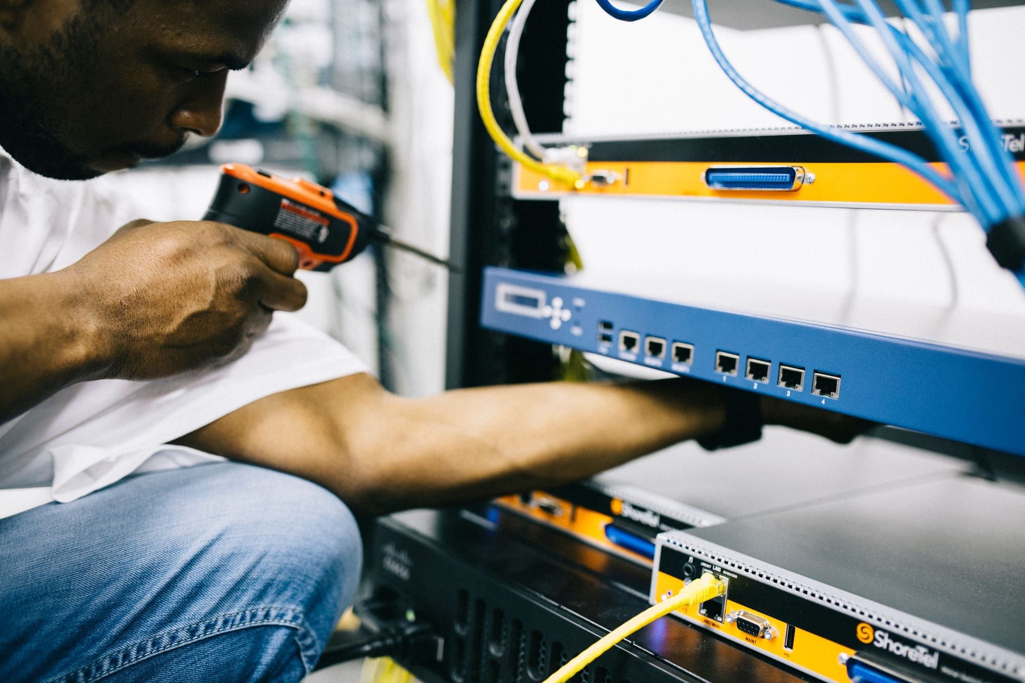 Técnico con un destornillador eléctrico montando equipos en un armario rack con cables conectados